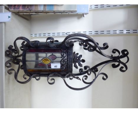 An early 20thC wrought black painted metal hanging lantern with clear and coloured lead glazed panels and twin C-scrolled orn