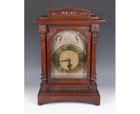 An early 20th century German oak mantel clock with eight day movement chiming on gongs, the silvered and brass arch dial with