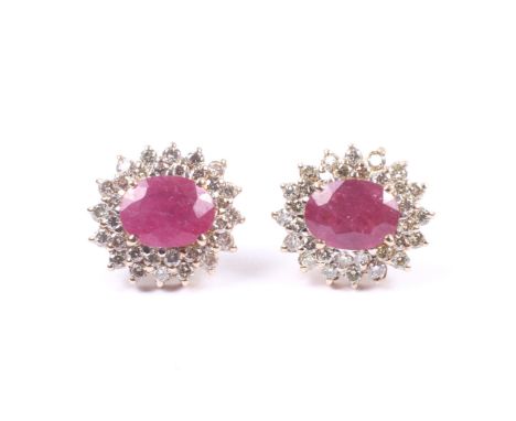 A pair of modern ruby and diamond oval cluster earrings. Each centred with a semi-opaque oval mixed-cut ruby within a round b