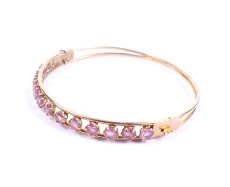 A vintage rose gold and ruby half-hoop hinged bangle. The open front claw set with 13 round mixed-cut pale rubies within tubu