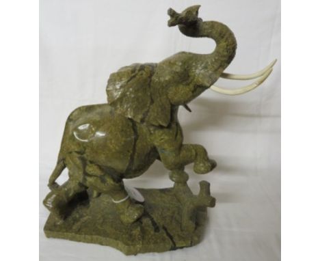 Shona style carved stone model of a bull elephant, one foot raised on log, a log in its trunk, variegated green stone, inscri