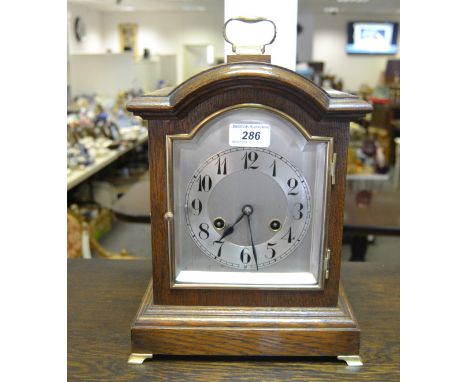 An oak mantel clock, twin winding holes, silvered dial, brass carry handle 