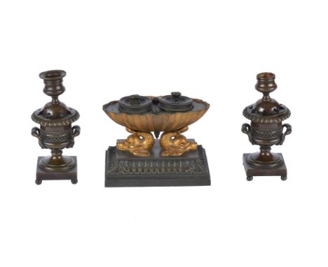 A Regency patinated and gilt bronze standish, circa 1820, the ink and pen holders enclosed in an oval shell, supported by twi