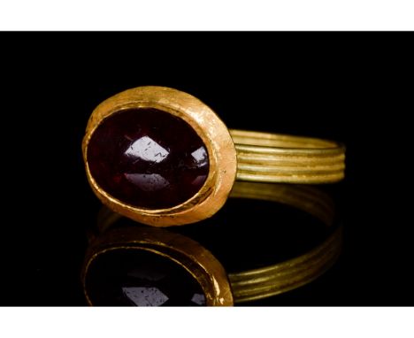 Ca. 200-400 AD. Late Roman. A wearable gold ring with an applied Roman oval bezel set with a cabochon garnet gem and a possib