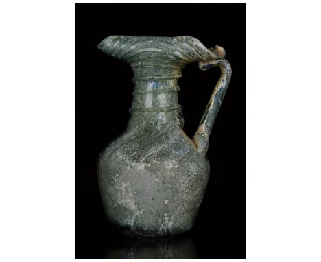 Ca. 300-400 AD. Late Roman. A dark-coloured glass jug with a near-spherical body, a cylindrical neck decorated with a spiral 