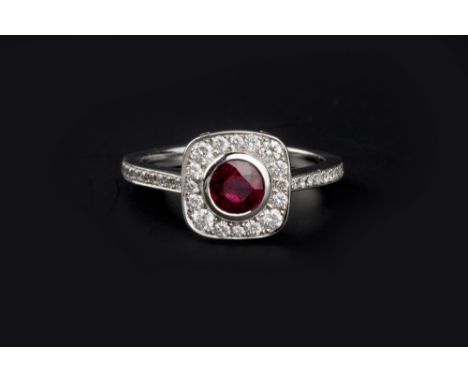 A RUBY AND DIAMOND CLUSTER RING, the circular mixed-cut ruby collet set within a cushion-shaped border of graduated round bri