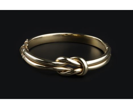 A YELLOW PRECIOUS METAL KNOT BANGLE, of hinged oval form, the clasp stamped '375', inner diameter 6cm