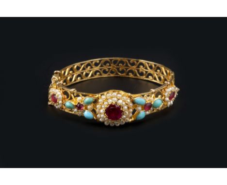 AN EASTERN VARI GEM-SET BANGLE, of hinged form, pierced with repeating scroll motifs, applied to the top with a red stone and