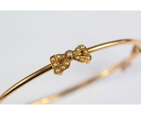 An Edwardian 15ct Yellow Gold Seed Pearl Bangle. The set with a seed pearl bow-form motif, approx 4.8 gms, approx 6 cms d tog