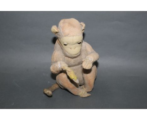An Alpha Farnell style seated monkey, having partial mohair covered body, amber glass eyes and holding a banana, height 16 cm
