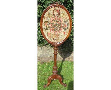 An early 19th century walnut tapestry pole screen, the oval tapestry in a frame with carved decoration, raised on a carved co