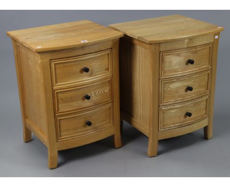 A pair of light-oak bow-front bedside chests each fitted three long drawers, 19¾” wide x 27” high x 18¼” deep.