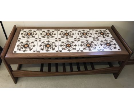 A retro tile topped coffee table with under shelf. Brown, cream and orange colouration. Approx. 118cm wide x 43 cm tall.