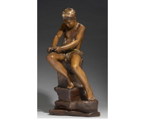A GOLDSCHEIDER PAINTED TERRACOTTA FIGURE OF A BOY, LATE 19TH C  designed by Lemoine,  seated on a rock sharpening an arrow, 5