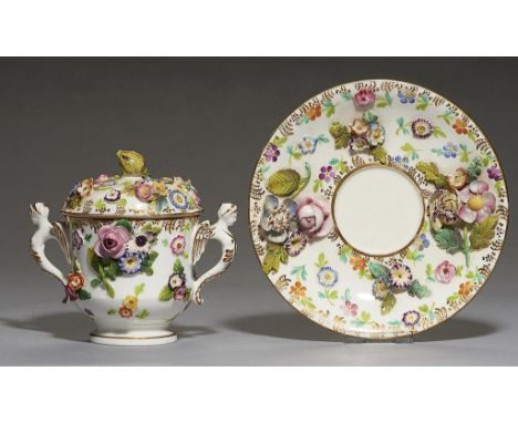 A STAFFORDSHIRE FLORAL ENCRUSTED CHOCOLATE CUP, COVER AND STAND, POSSIBLY SPODE, C1825 with gilt winged demi figure handles, 