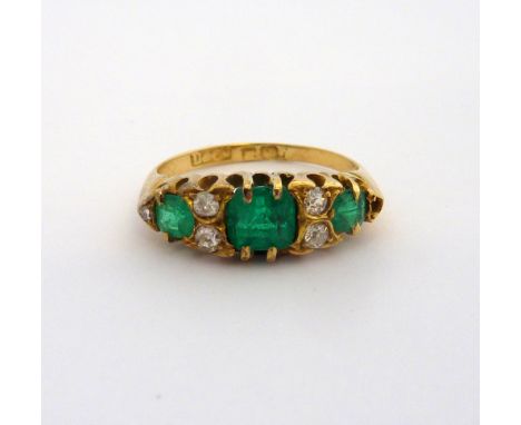 AN EMERALD AND DIAMOND RING, with three graduated cushion cut emeralds with old cut diamond accents to the plain tapered shan
