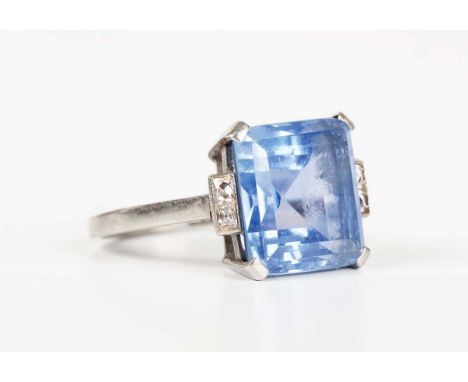 A platinum, diamond and synthetic sapphire ring, claw set with the square cut synthetic sapphire between diamond two stone sh