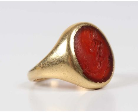 A gold and cornelian intaglio signet ring, designed as a lady wearing a crown above two crossed quills/feathers, indistinct m
