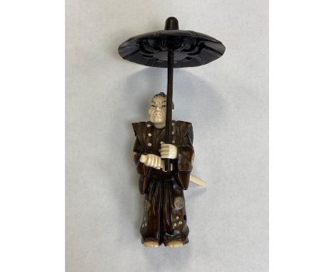 A carved Japanese netsuke modelled as a figure with parasol holding a sword, height 10 cm.