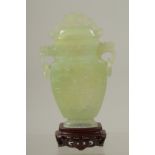 A CHINESE CARVED JADE LIDDED VASE AND WOODEN STAND, the vase with archaic style carving and drop