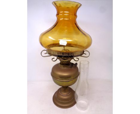 An antique brass oil lamp with amber glass shade and chimney 