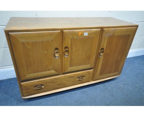 AN ERCOL BLONDE ELM SIDEBOARD, with double cupboard doors over a single drawer flanked by a single cupboard doors, on casters