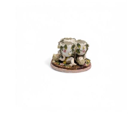 A Sitzendorf porcelain figural table centrepiece, modelled as three reclining putti, each holding a floral encrusted egg shel