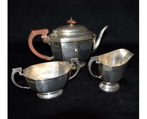 A SILVER THREE PIECE TEA SET The plain form tea set with canted corners on pedestal base composition handle and knop to teapo