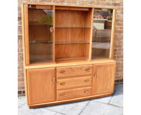 A MODERN LIGHT ERCOL DRESSER  the upper section with adjustable glass shelves flanked by glazed cupboards, the base with thre