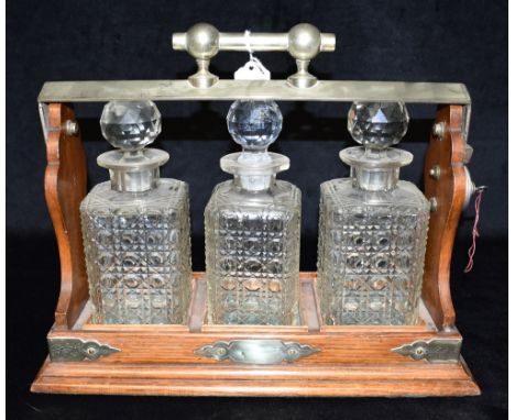 AN EDWARDIAN EPNS MOUNTED OAK FRAMED THREE BOTTLE TANTALUS stamped 'JBC &amp; S l' within a crescent, for J B Chatterley and 
