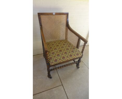 An early 20th century beech and cane single bergere armchair with drop in seat, bobbin turned stretcher and raised on castors