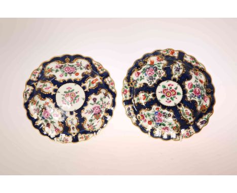 A PAIR OF WORCESTER SCALE BLUE GROUND SCALLOPED PLATES, CIRCA 1770, enamelled with panels of flowers, square seal marks. 19cm