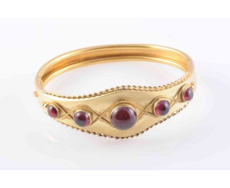 A MID VICTORIAN GARNET SET BANGLE, the five graduating round cabochon cut garnets set evenly spaced to the centre of a taperi