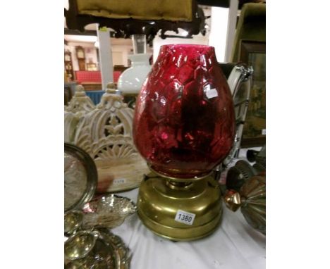 A brass oil lamp with cranberry glass shade