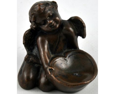 A bronzed ring stand, modelled as a seated putto holding a heart shaped bowl