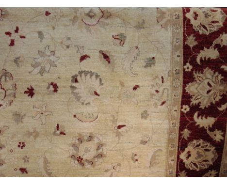 A large wool carpet in the Persian style, the pale cream field set within a burgundy coloured border with repeating floral de