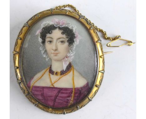 A Victorian pinchbeck framed mourning brooch depicting a bust portrait of a maiden wearing a lace bonnet and garnet necklace,