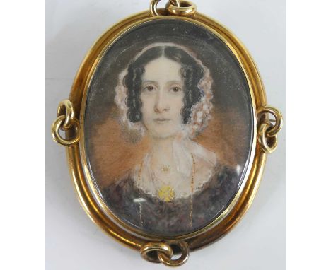 A Victorian miniature portrait mourning brooch, depicting a bust portrait of a woman wearing a lace bonnet and long guard cha