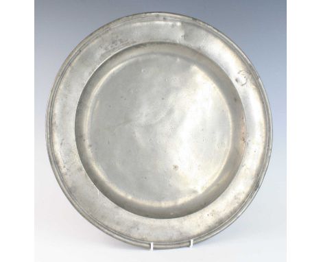 An early 18th century pewter charger, having a wide single-reeded rim bearing several touch marks, initials and armorial, glu