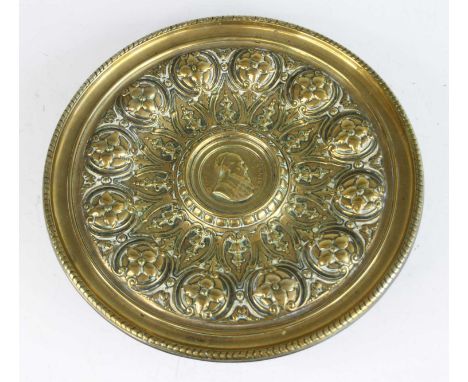 A late 19th century continental brass pedestal alms dish, the centre decorated with a portrait roundel within leaf and flower