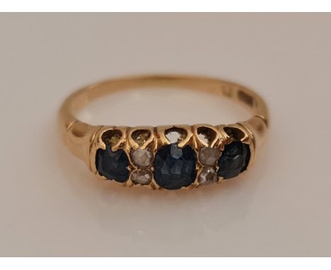 A sapphire and diamond ring, set with three oval cut sapphires separated by four rose cut diamond accents, unmarked yellow me