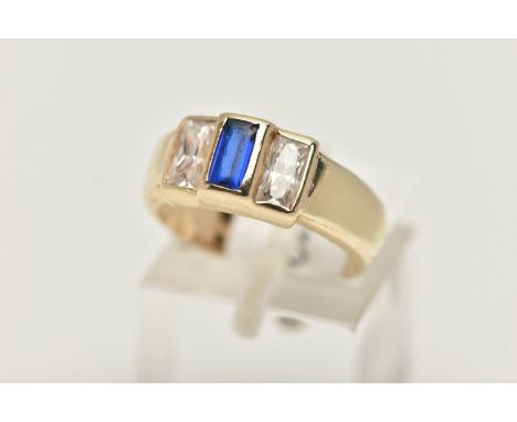A YELLOW METAL CUBIC ZIRCONIA RING, set with one blue and two colourless cubic zirconia stones, wide polished band, stamped 5