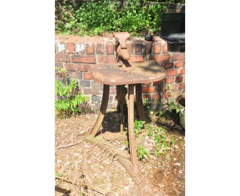 A VINTAGE CAST IRON LEG VICE ON STAND with a triform swept leg base and Demi lune top width 53cm depth 57cm and height 96cm C