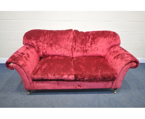 A RED VELVETEEN UPHOLSTERED TWO SEATER SETTEE, on turned legs and brass casters, length 202cm x depth 94cm x height 96cm (con