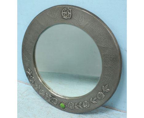 An Arts &amp; Crafts style circular mirror, with silver hammered decoration, floral swags, green coloured stone and central C