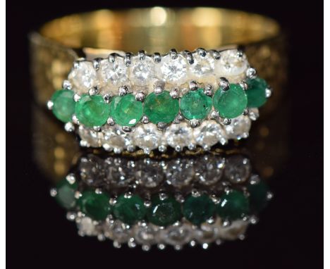 An 18ct gold ring set with a row of emeralds and two rows of diamonds with textured shoulders, 9.1g, size W/X&nbsp;