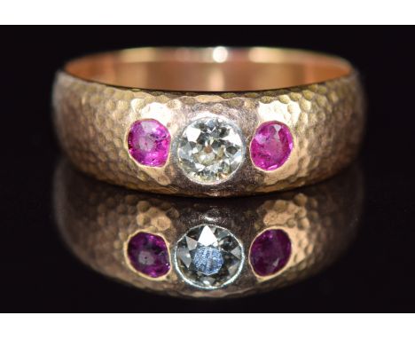 A 9ct gold ring with hammered decoration set with an old cut diamond of approximately 0.25ct and two rubies, 4.3g, size M