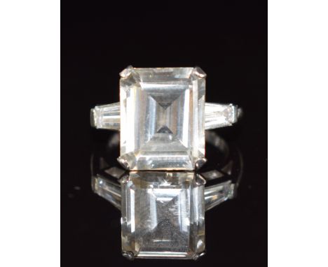 A 14k white gold ring set with an emerald cut white sapphire and baguette cut white topaz to each shoulder, 4.8g, size I