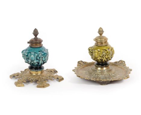 Two Linthorpe Pottery Inkwells, moulded with the faces of cherub, in green and turquoise glaze, brass mounted bases and cover