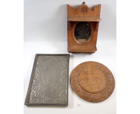 A wooden bread board carved 'Manners Maketh the Man' a pewter embossed tray and a wooden shelf with mirror 